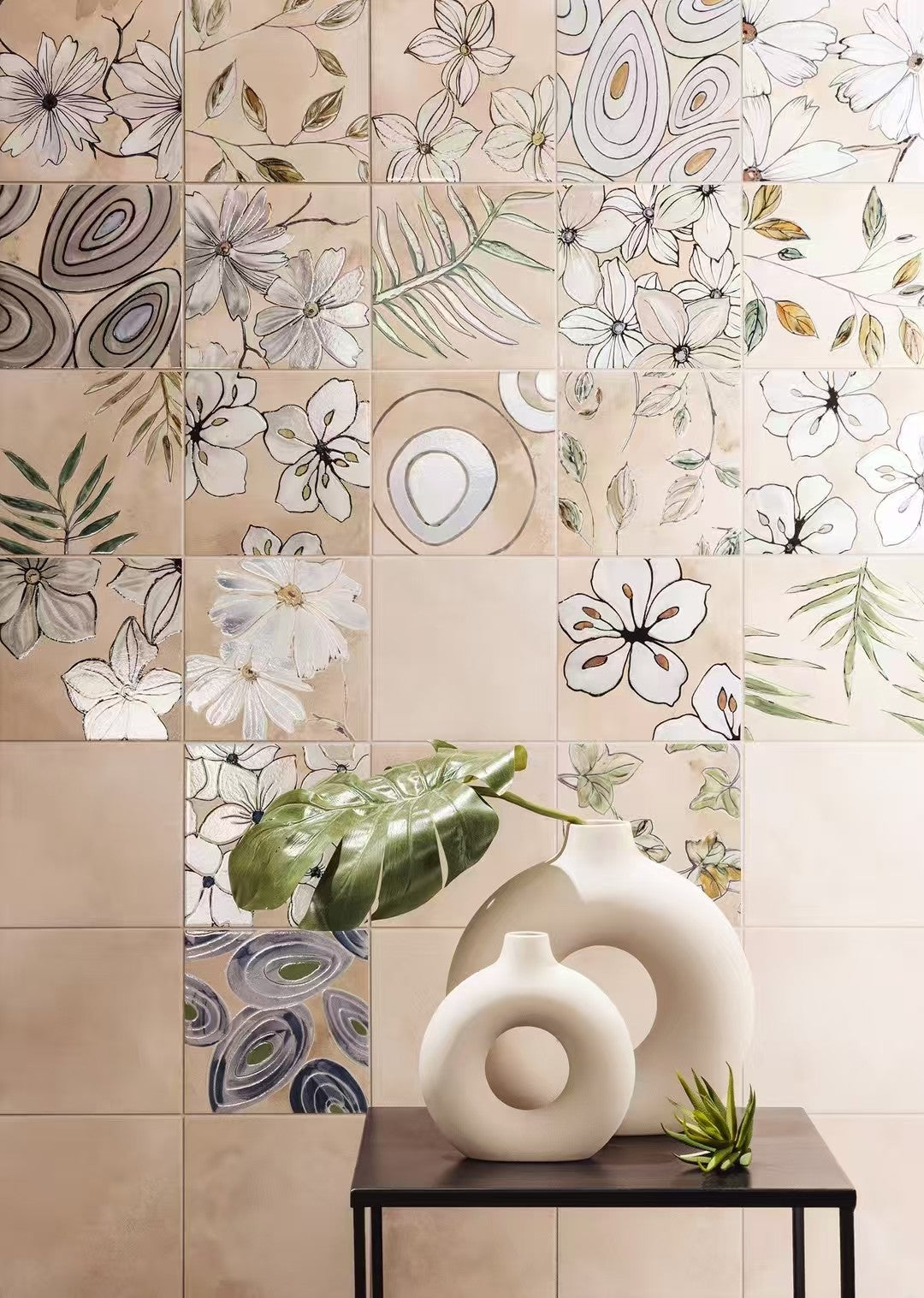 Decorative tiles with floral and abstract patterns on a wall with vases and plants below.