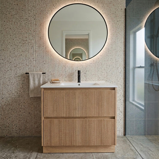 Fluted oak floor standing vanity with integrated ceramic basin and matte black tapware, shown with round LED mirror and terrazzo wall tiles — available in 600mm to 1200mm, The Tile Collection NZ