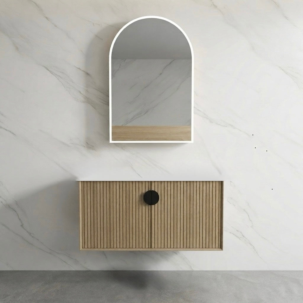 A modern wall-mounted bathroom vanity with a slatted wood cabinet and a round black handle, paired with an arched wall mirror above, set against a white marble wall.